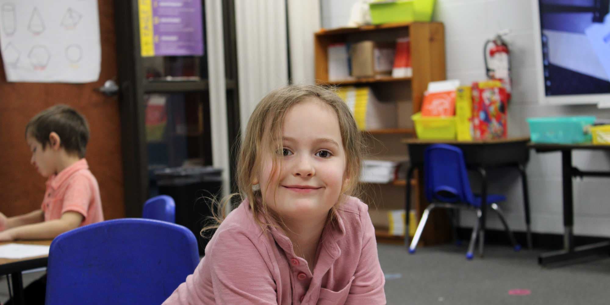 Smiling student sitting at a desk in a classroom.