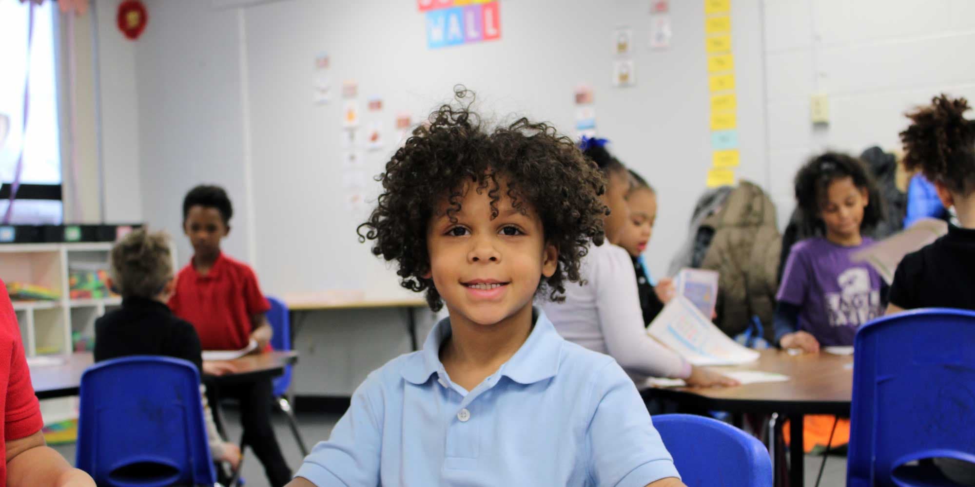 Smiling student sitting in a busy classroom with classmates.