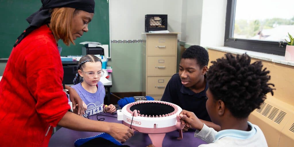 An instructor guiding Toledo Prep students using a knitting machine