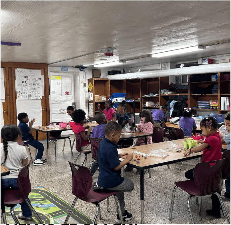 Children at tables in a classroom, playing with small objects.