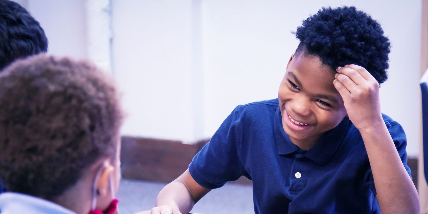 Students smiling as they play checkers in a classroom.